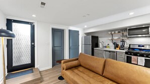 A modern kitchen with a stainless steel stove, microwave, and refrigerator. There is a brown leather sofa in the living area.