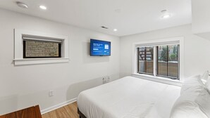 A modern bedroom with a large bed, a television mounted on the wall, and a window providing a view of the outdoors.