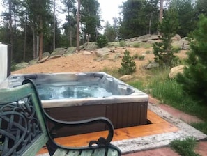 Ein Whirlpool mit Holzterrasse und Metallbank, eingebettet in eine natürliche Landschaft mit Bäumen und Felsen.