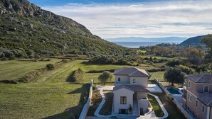 Ein zweigeschossiges Haus mit befestigter Auffahrt und Swimmingpool, umgeben von grünen Feldern und Hügeln.