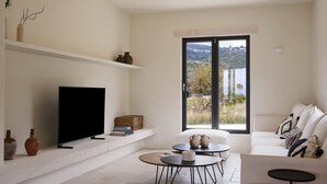 Ein modernes Wohnzimmer mit einem Flachbildfernseher, einem Sofa, einem Couchtisch und einem großen Fenster mit Blick auf die Landschaft.