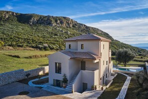 Une maison moderne à deux étages, dotée d’un mur en pierre, d’une piscine et offrant une vue sur un paysage montagneux.