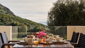 Ein Esstisch, gedeckt für ein Frühstück, mit schöner Aussicht auf Hügel und Bäume.