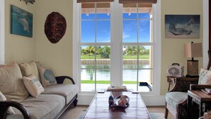 Un salon avec vue sur un lac, un canapé agrémenté de coussins décoratifs, une table basse avec un saladier, et un fauteuil.
