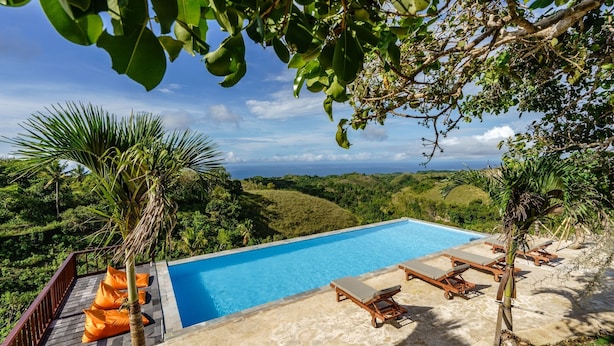 A pool with lounge chairs, surrounded by greenery and a view of the landscape. - Deluxe Bungalow with Bathtub, Pini Sentana Village (Nusa Penida)