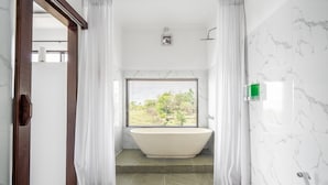 A modern bathroom with a freestanding bathtub, a window with blinds, and a shower area. - Deluxe Bungalow with Bathtub, Pini Sentana Village (Nusa Penida)