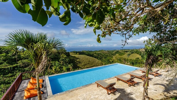 A pool with lounge chairs, surrounded by greenery and a view of the landscape. - Deluxe Bungalow with Terrace, Pini Sentana Village (Nusa Penida)