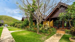 A residential property with a well-maintained lawn, a paved driveway, and a wooden house with a porch. - Deluxe Bungalow with Terrace, Pini Sentana Village (Nusa Penida)