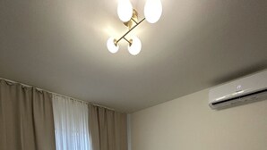 Et soveværelse med seng, gardiner, en aircondition og en lampe i loftet.