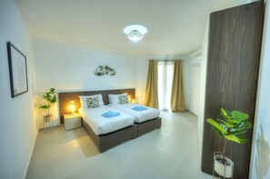 Quarto de hotel moderno com uma cama de casal, mesas de cabeceira, um vaso de plantas e uma janela grande com cortinas.