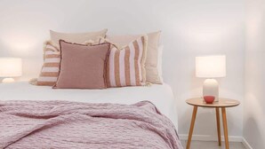 A neatly made bed with a pink blanket, two bedside lamps, and a small round table with a bowl. - Casienda (Casuarina)