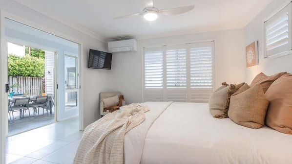 A bedroom with a bed, a ceiling fan, a TV, and a sliding glass door leading to an outdoor area.