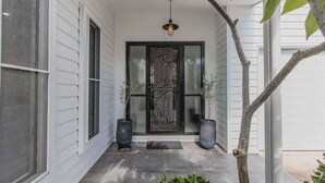 A house entrance with a black decorative door, two potted plants, and a hanging light fixture. - Casienda (Casuarina)