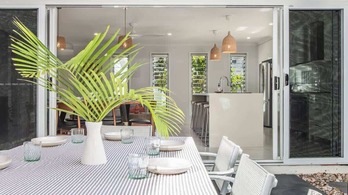 A modern dining area with a striped tablecloth, white chairs, and a large potted plant.