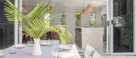 A modern dining area with a striped tablecloth, white chairs, and a large potted plant.