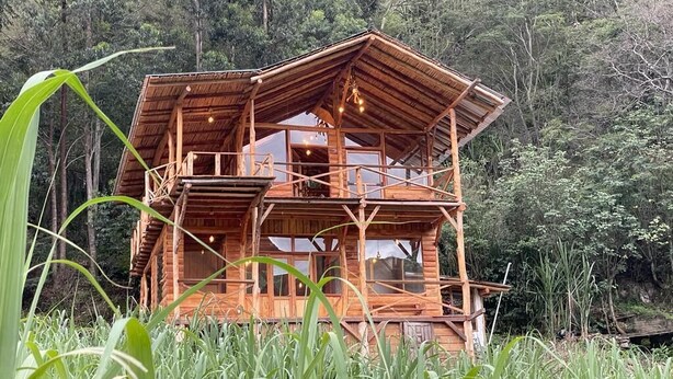 A wooden cabin with multiple balconies, surrounded by lush greenery. - Eco-Finca Hostal Santorum (Vilcabamba)