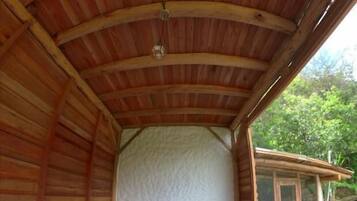 Una stanza circolare in legno con un letto, una finestra e vista sul verde all'esterno.