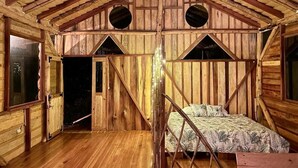 A rustic wooden cabin with a lofted sleeping area and a door leading outside. - Eco-Finca Hostal Santorum (Vilcabamba)
