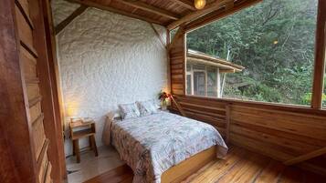 Una camera da letto accogliente con soffitto in legno e un'ampia finestra con vista su una zona boschiva.