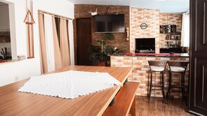 A modern kitchen with a brick wall, a flat-screen TV, and a bar area with stools. - Refúgio na Praia do Campeche com Piscina (Florianópolis)