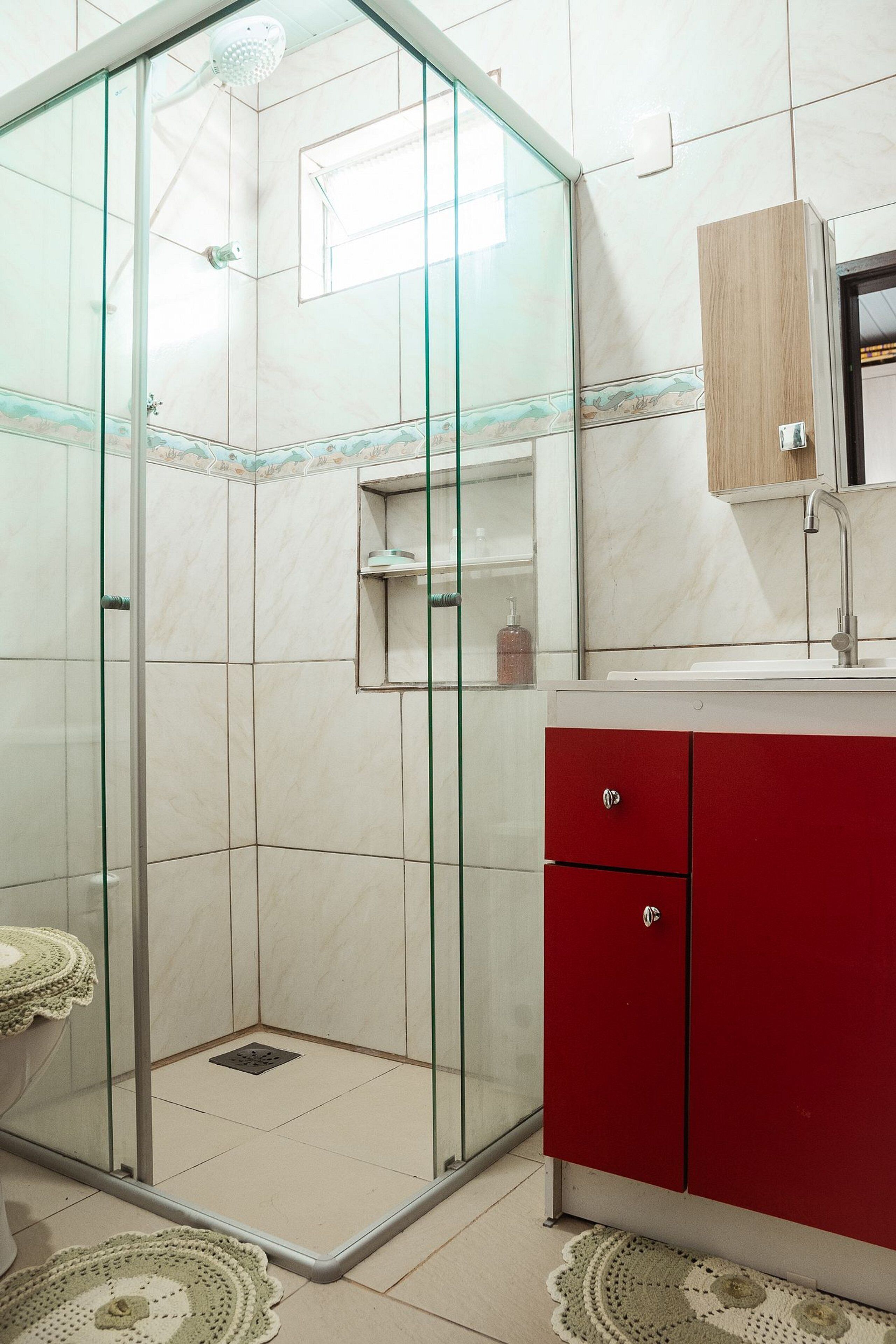 Casa de banho com cabine de chuveiro em vidro, um armário vermelho e uma pia com espelho em cima.