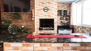 A kitchen with a brick wall, a flat-screen TV, a fireplace, and a countertop with a red mat. - Refúgio na Praia do Campeche com Piscina (Florianópolis)
