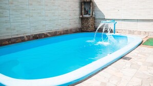 A swimming pool with a wooden sign above it, a small shrine-like structure, and a stone wall. - Refúgio na Praia do Campeche com Piscina (Florianópolis)