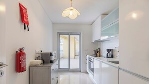 A modern kitchen with white cabinets, a coffee machine, and a fire extinguisher on the wall. - Sea Sound Apartment (Sesimbra)