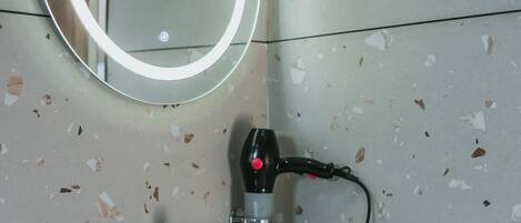 A bathroom with a white sink, a round mirror with a light, and a hairdryer on the wall.