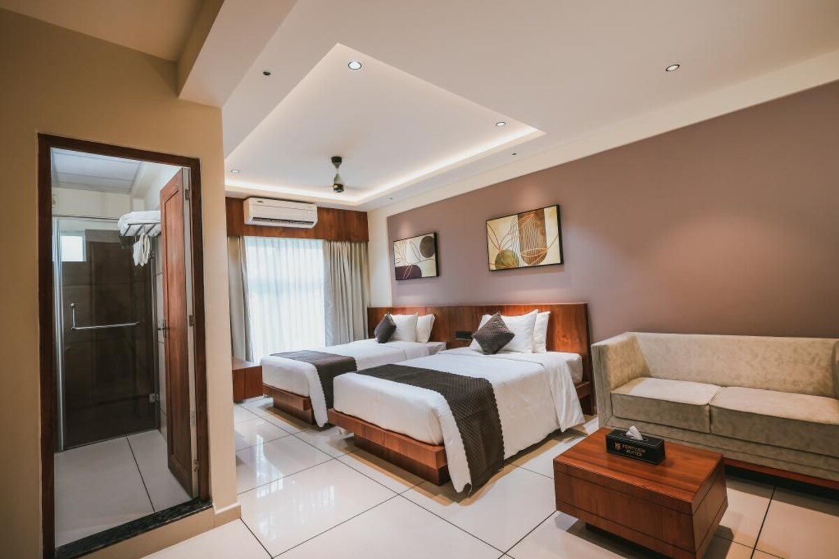 A hotel room with two beds, a sofa, a coffee table, and an air conditioning unit.