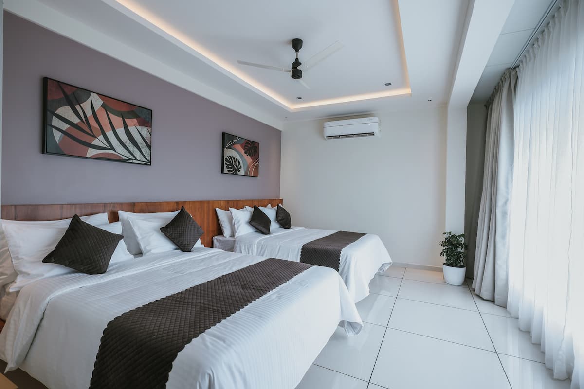 Habitación de hotel con dos camas, ventilador de techo, equipo de aire acondicionado y una planta en maceta.
