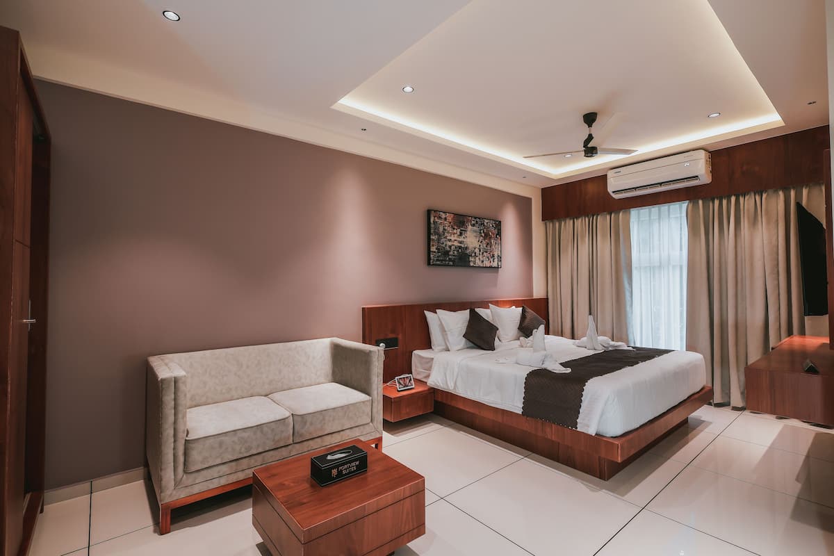 Una habitación de hotel moderna con una cama grande, un sofá, una mesita de noche de madera y un ventilador de techo.