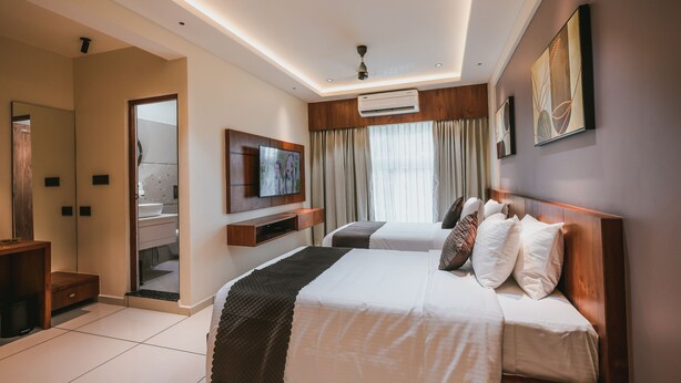 Une chambre d’hôtel moderne, dotée d’un grand lit, d’une télévision et d’une salle de bain visible à travers une porte ouverte.