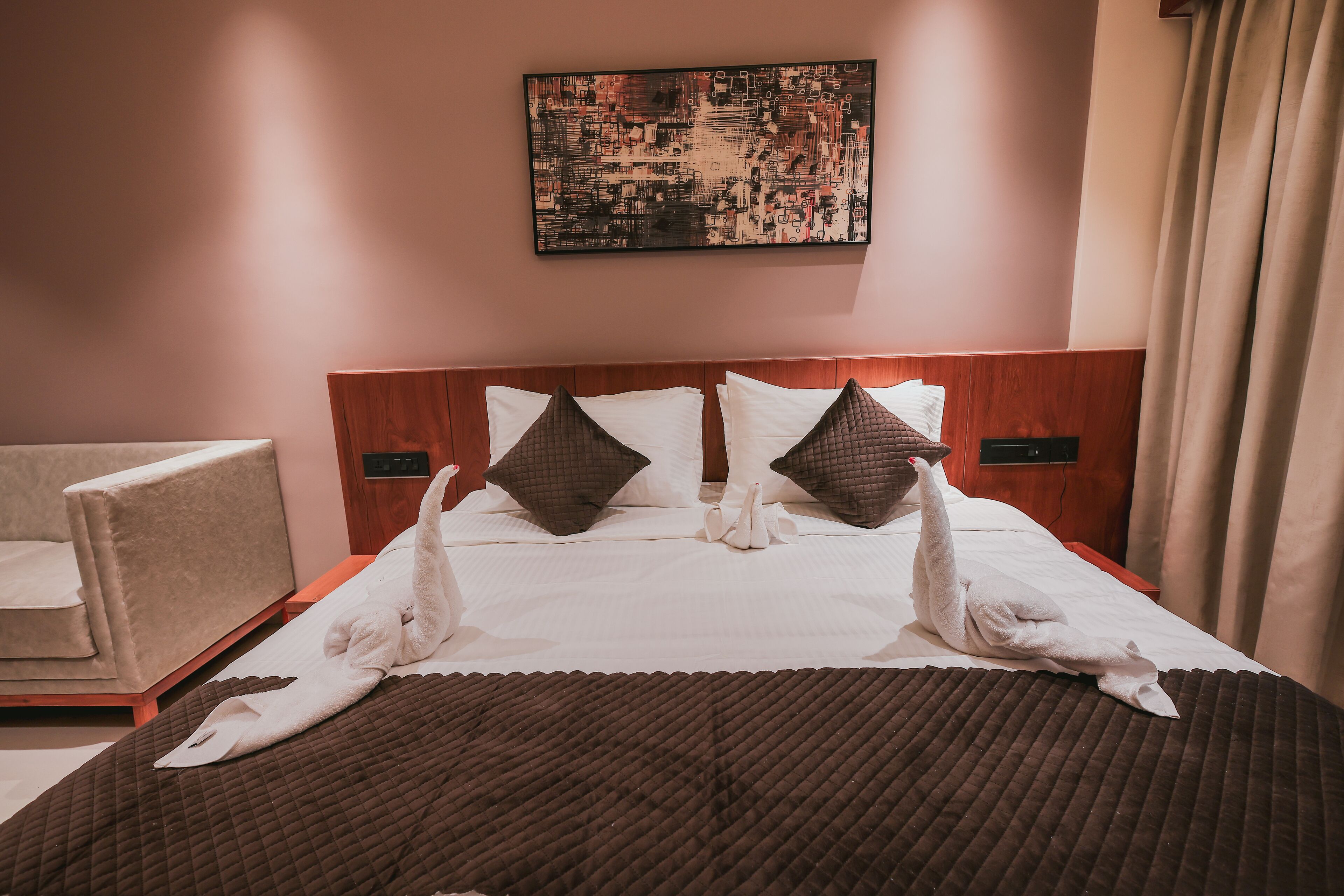 A hotel room with a bed, two pillows, a blanket, a chair, and a wall-mounted artwork.