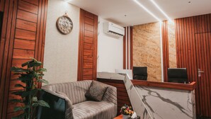 Un espace d’accueil moderne comprenant un comptoir de réception en marbre, un canapé, une table basse et une plante en pot.