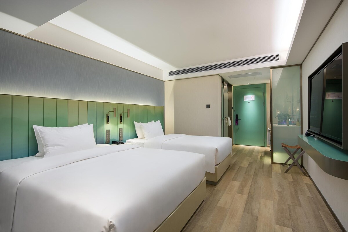 A hotel room with two beds, a TV, and a bathroom visible through a door.