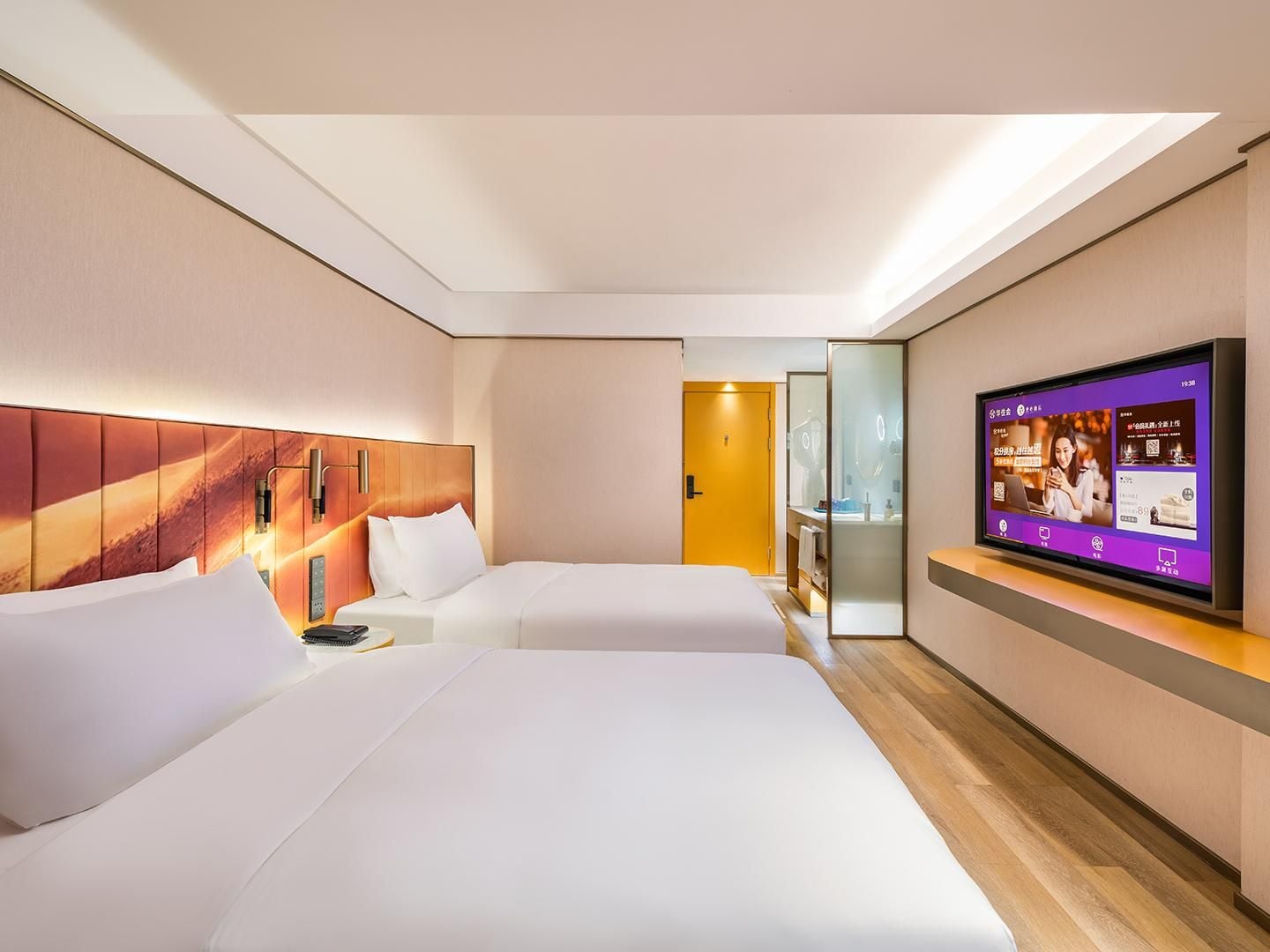 A hotel room with two beds, a TV on the wall, and a wooden floor.