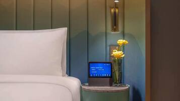 Una habitación de hotel con una cama, una mesita de noche con un teléfono inteligente y un jarrón con flores.