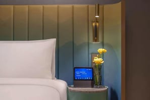 Una habitación de hotel con una cama, una mesita de noche con un teléfono inteligente y un jarrón con flores.