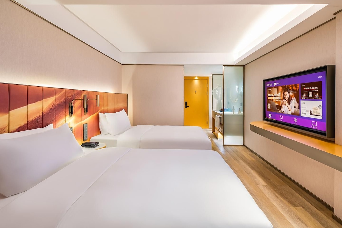 Habitación de hotel con dos camas, un televisor en la pared y suelo de madera.
