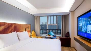 Habitación de hotel con una cama grande, televisión, balcón con cortinas y vista a la ciudad.