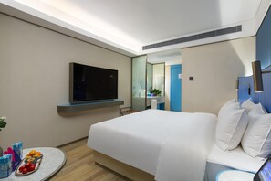 A hotel room with a bed, a flat-screen TV mounted on the wall, a round table with fruits and a bottle, and a bathroom visible through a glass door. - Manxin Hotel Changsha IFS (Changsha)