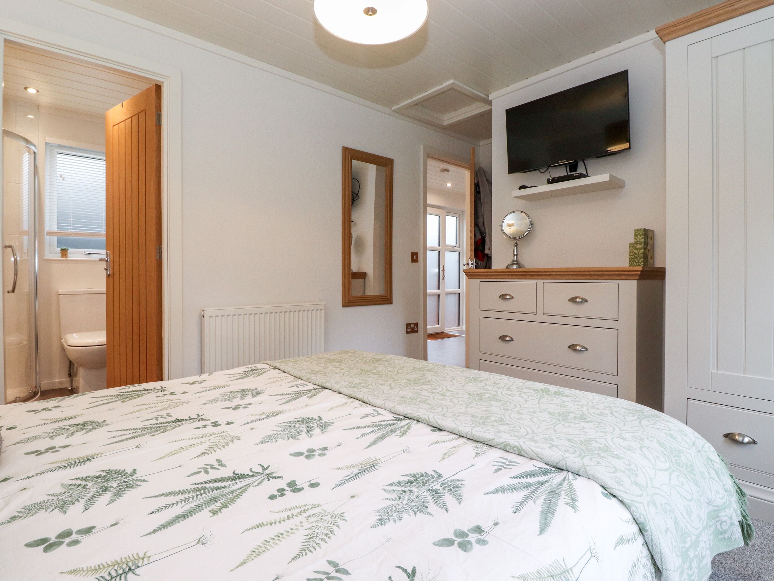 A bedroom with a bed, a dresser, a mirror, and a television on the wall.
