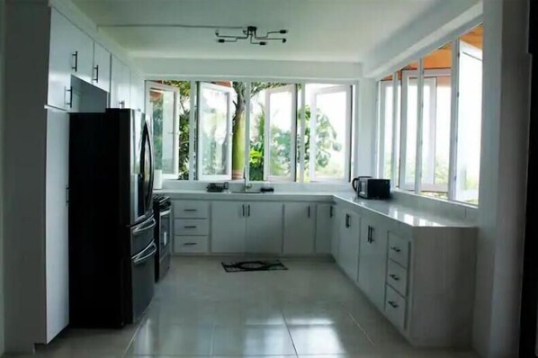 A modern kitchen with white cabinets, a black refrigerator, and a window with a view of greenery. - Caribbean Sea View 2 Beds 2 Bath (Castries)