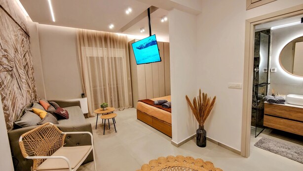 Une chambre d’hôtel moderne comprenant un canapé, une petite table ronde, un lit, une télévision, une salle de bain avec un miroir et un vase décoratif.