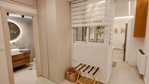 Une salle de bain moderne avec un meuble-lavabo, un miroir rond, une fenêtre avec des stores et un petit banc en bois.