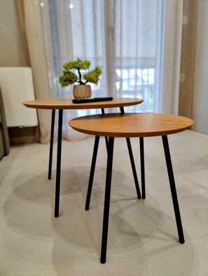 Two wooden tables with black legs in a room with a tiled floor and a potted plant on one table. - Elpis' cozy & luxury apartment (Egaleo)