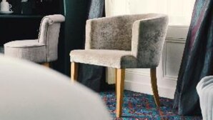 A room with a patterned carpet, a grey upholstered chair, and a dark-colored wardrobe. - The Gregory by Warren Collection (Belfast)