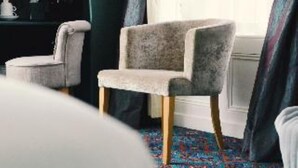 A room with a patterned carpet, a grey upholstered chair, and a dark-colored wardrobe. - The Gregory by Warren Collection (Belfast)