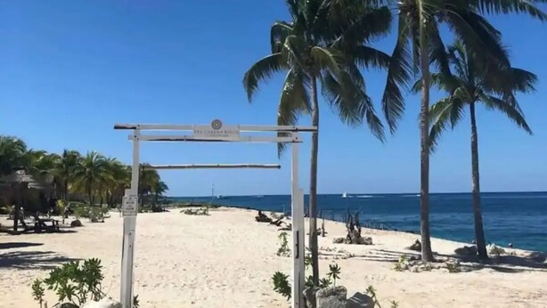 Uma praia com um arco branco, palmeiras e um céu azul límpido.